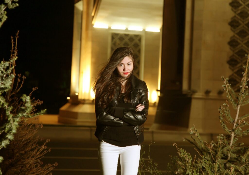 A woman standing in front of a building at night.