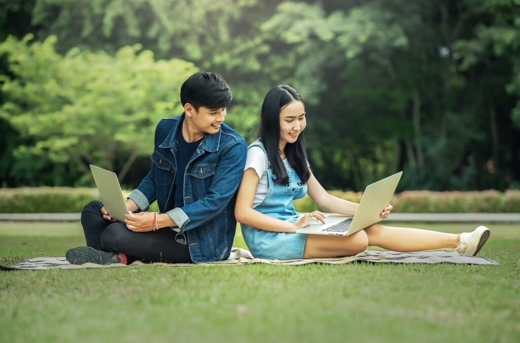 Two people sitting on a blanket with laptops