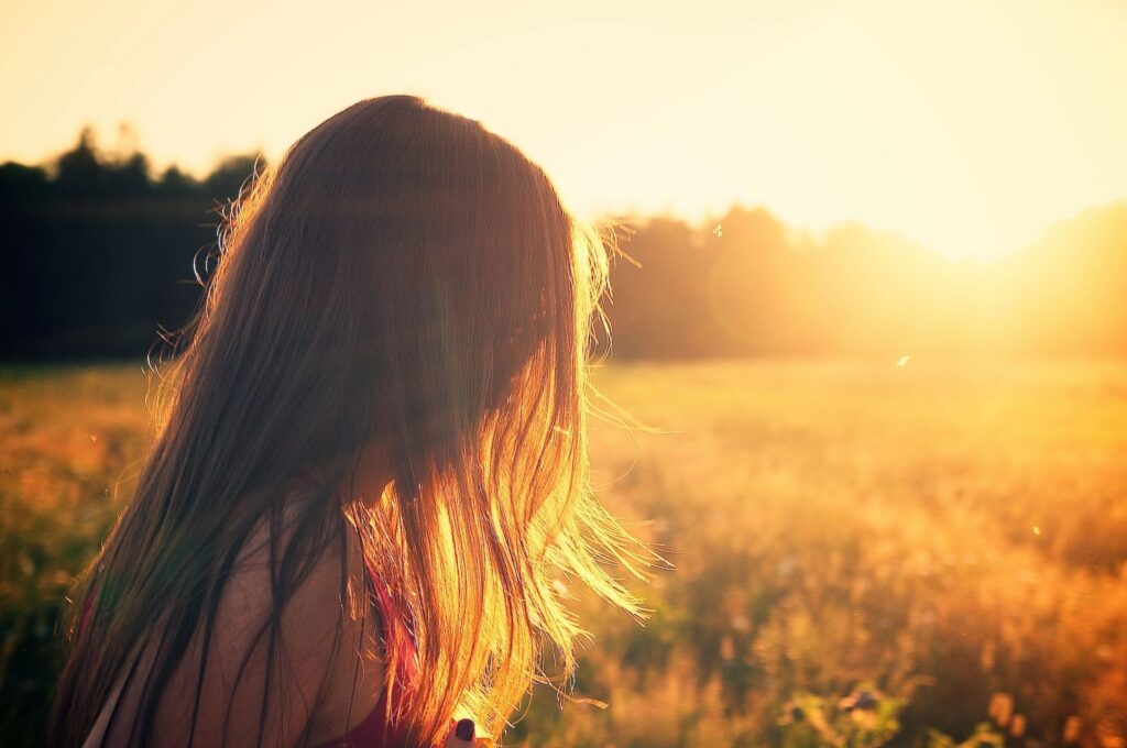 A woman standing in the middle of a field at sunset.